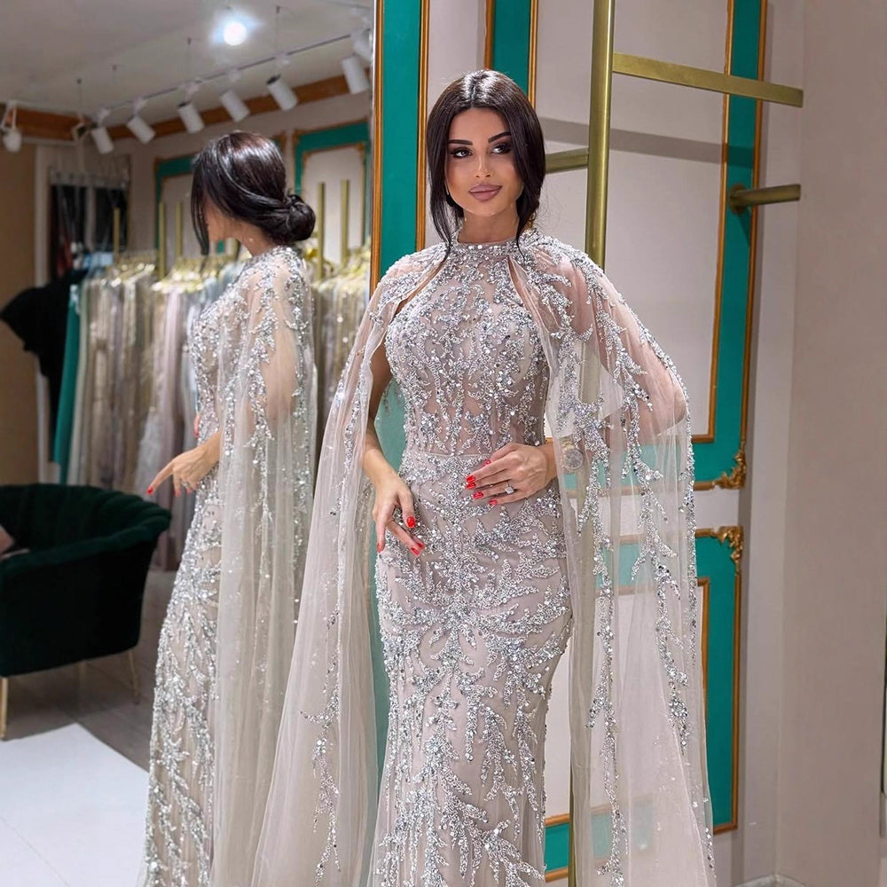 Woman wearing a sparkling beaded caramel Arabic style dress with a cape sleeves in a store setting.